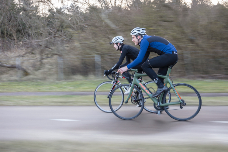 Twee wielrenners fietsen over weg langs bos, foto Alliander