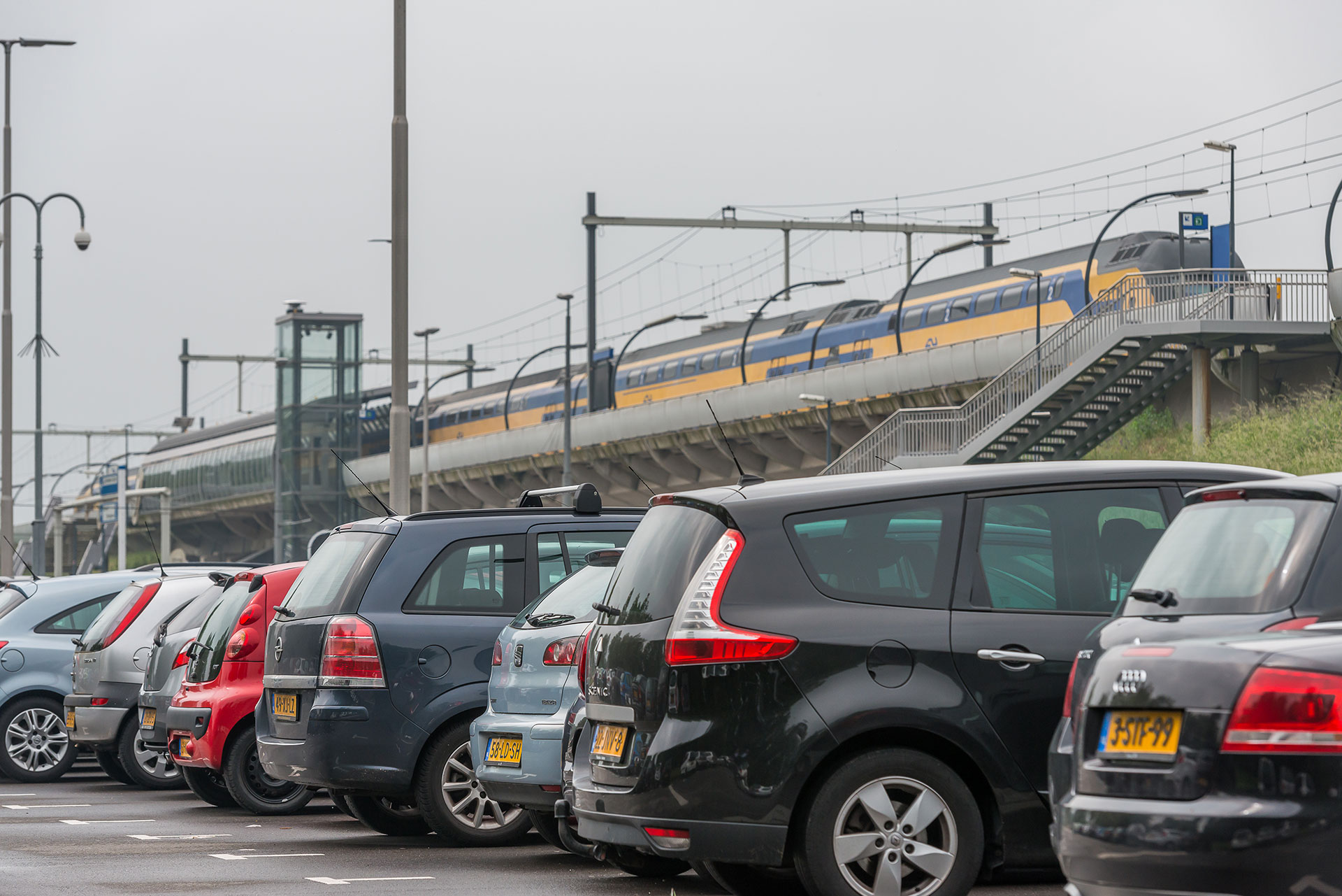 Auto's geparkeerd bij een station terwijl een trein langs komt rijden